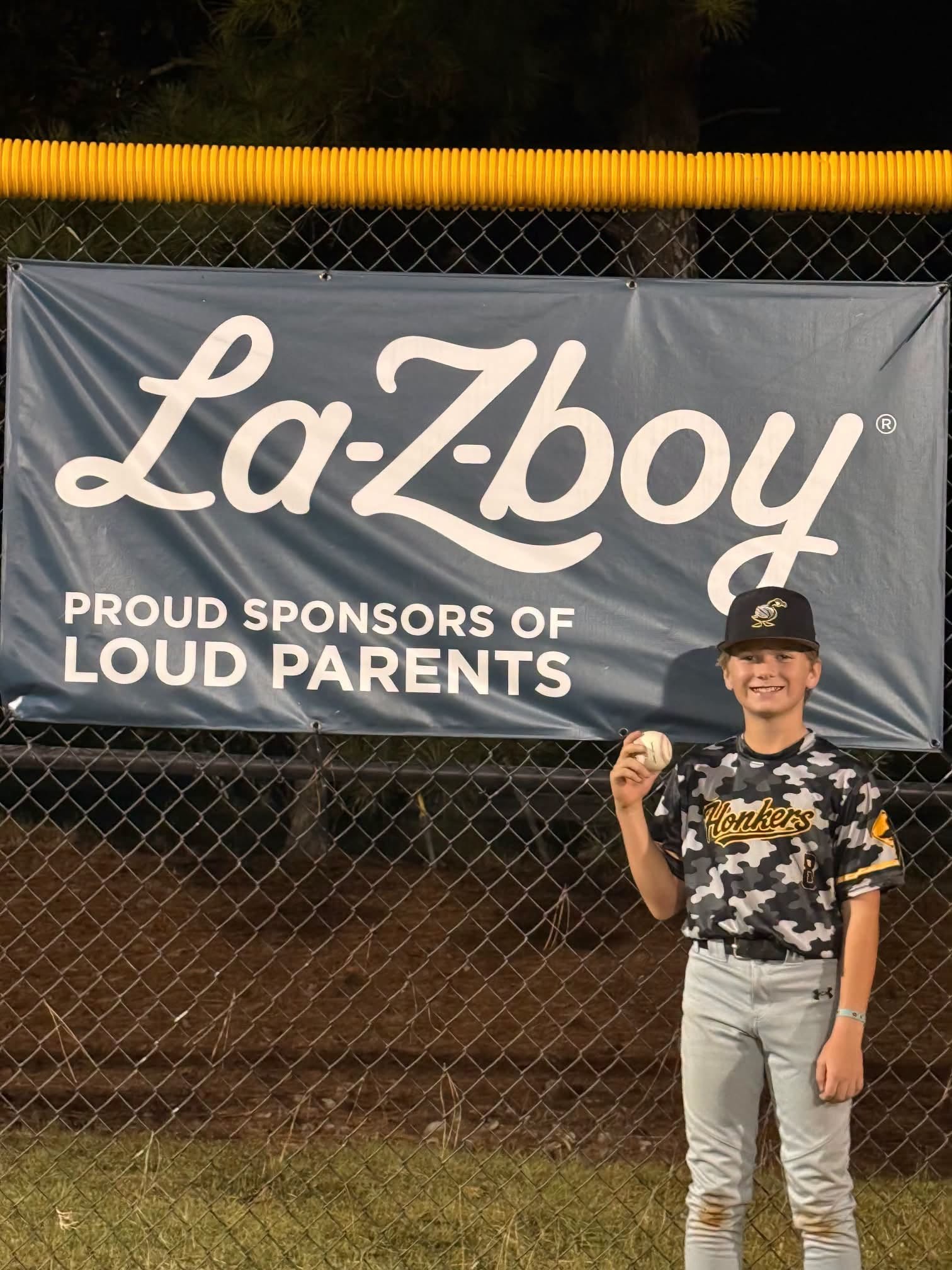 Harris Evans holding his homerun baseball in front of the La-Z-Boy banner at American Little League